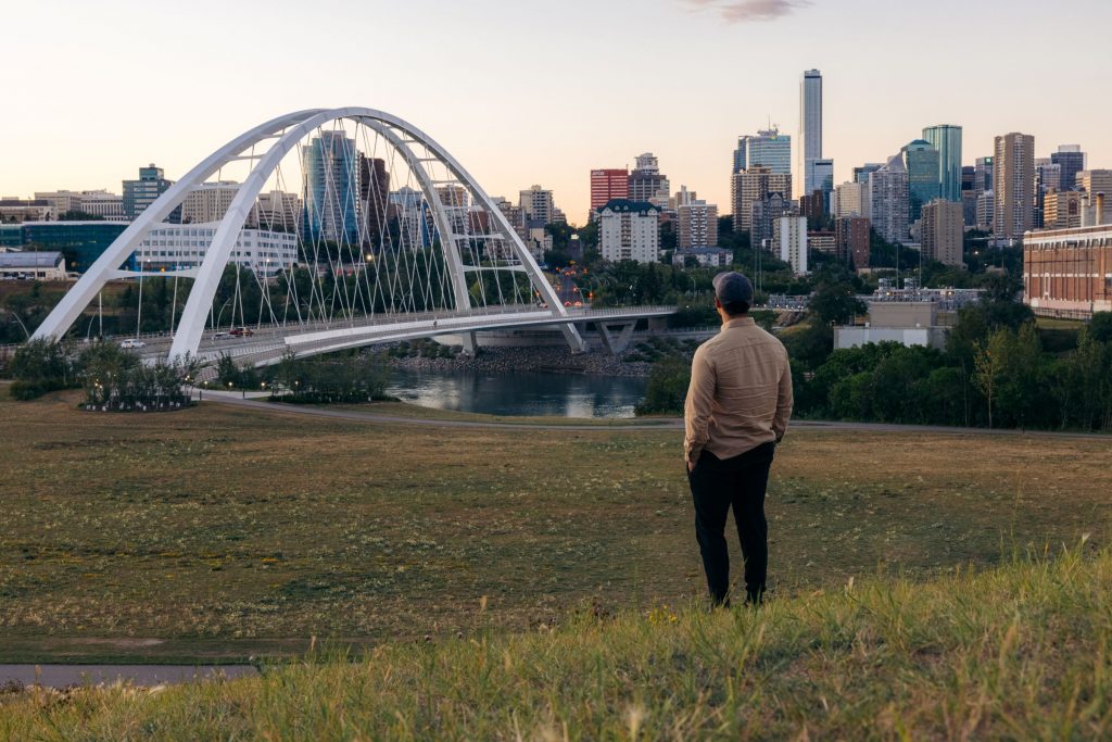 This image has an empty alt attribute; its file name is Walterdale-Park_Man-looks-at-Walterdale-Bridge-with-city-skyline-in-background-1024x683.jpg